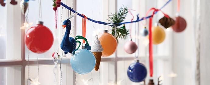 Garland with colorful baubles, bird, and ice cream ornaments hanging in front of a window.