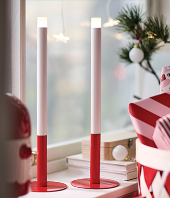 Two slim white and red LED candles on a decorated windowsill.