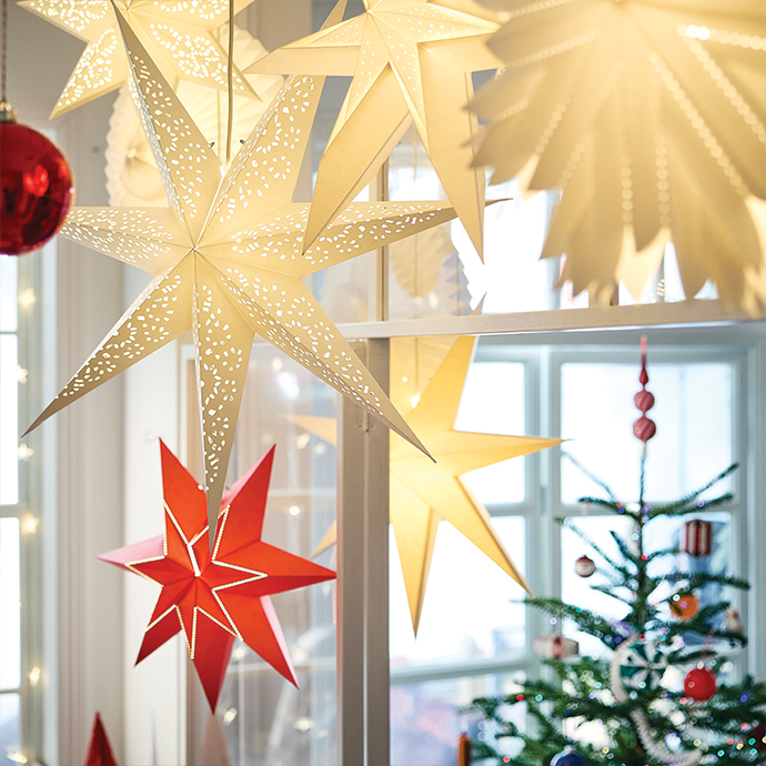 Luminous paper star lamps hanging near a decorated Christmas tree.