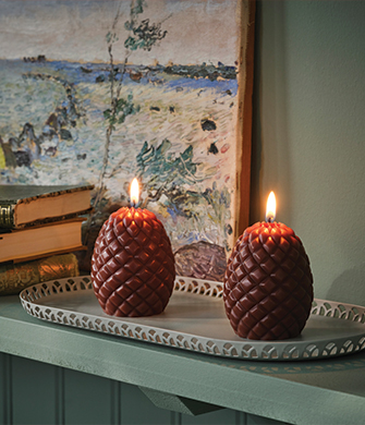 Two lit pinecone-shaped candles placed on a decorative tray.