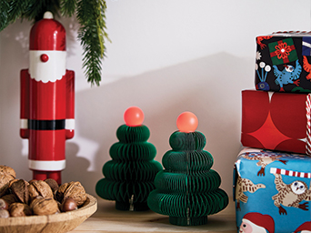 Paper Christmas tree ornaments, a red nutcracker, and wrapped gifts on a table.