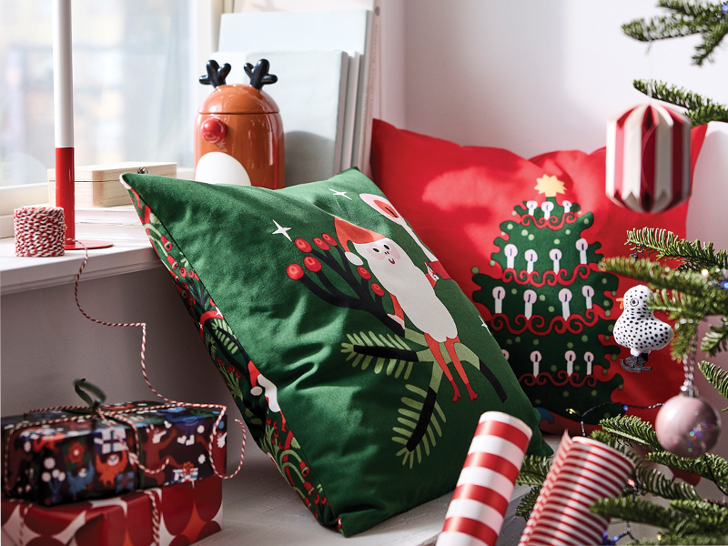 Festive green and red Christmas cushions next to a decorated window setting.