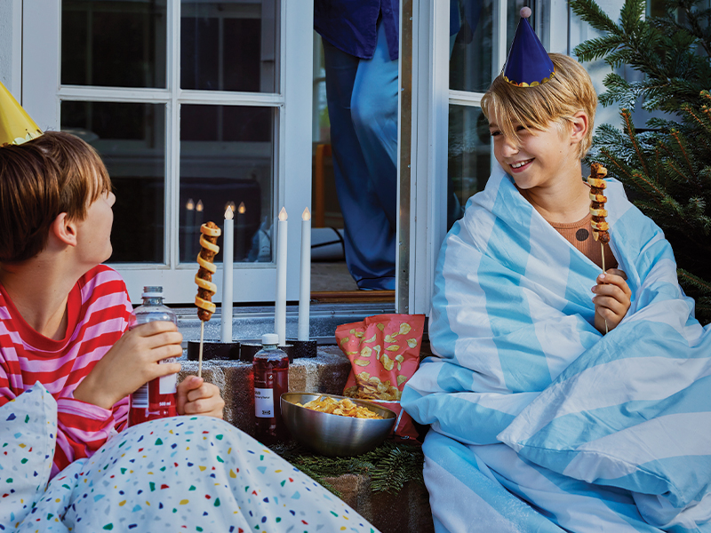 Kids with party hats wrapped in blankets enjoying snacks outside.