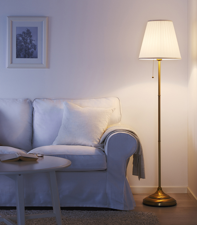 Cozy living room corner with a brass floor lamp casting warm light beside a white sofa with neutral cushions and a coffee table.