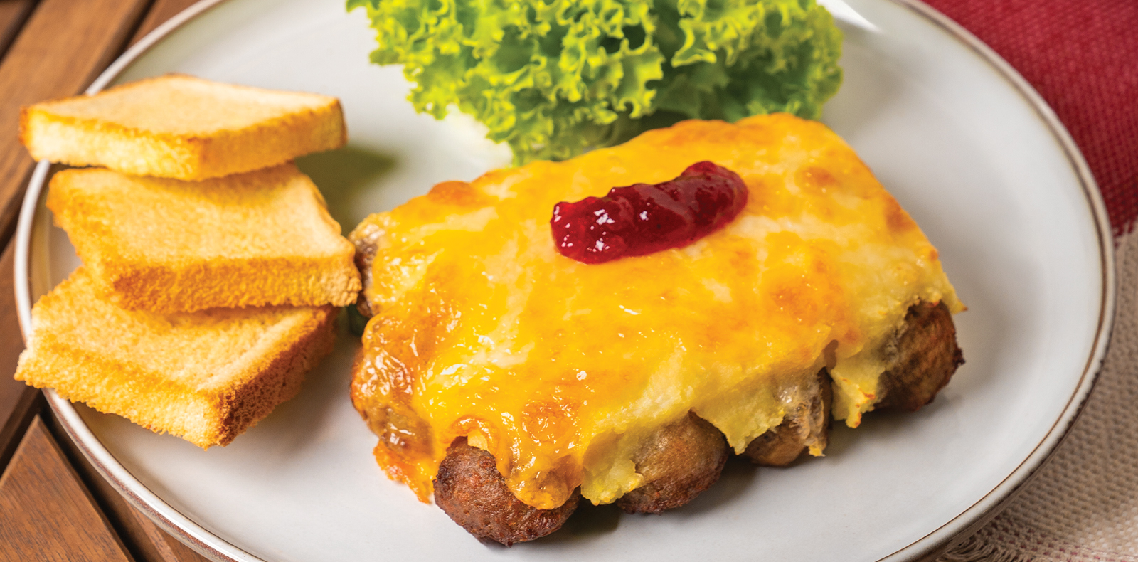 Plate of baked meatballs with melted cheese, jam, toast, and fresh lettuce.