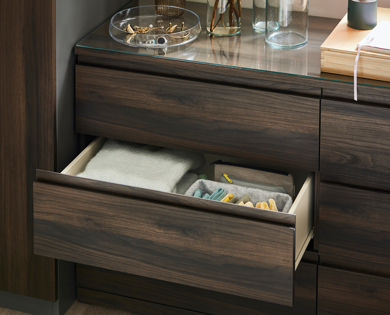 Open drawer of dark dresser organized with folded clothes and accessories.